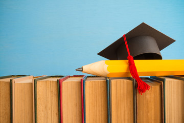 Graduation cap and big pencil over the books on blue wall background - Education concept