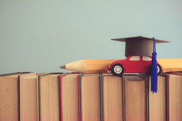 Graduation cap, wooden car and big pencil over the books on blue wall background - Education concept