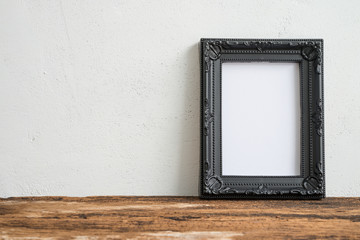 Black vintage photo frame on old wooden table over white wall background