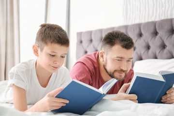Fototapeta premium Little boy and his dad reading books in bedroom