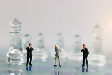 Miniature people, businessman with glass chess standing on chessboard. Concept of Strategy with thinking and intelligence challenge.