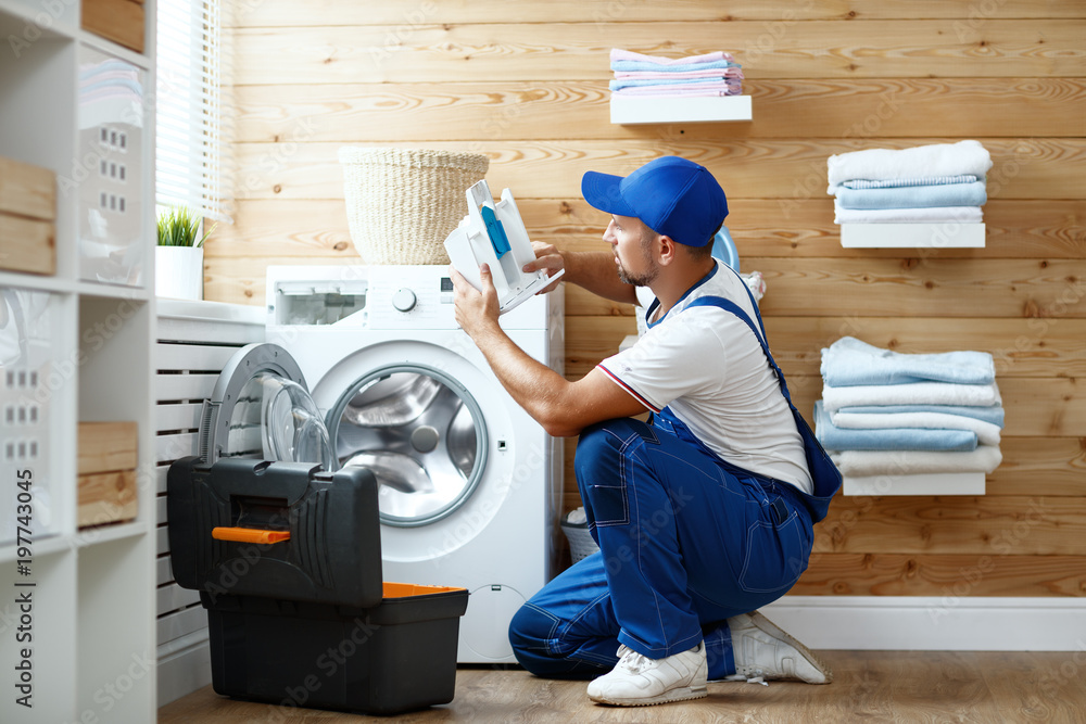 Wall mural working man plumber repairs washing machine in laundry.