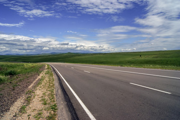 Empty asphalt road through the green field and blue sky