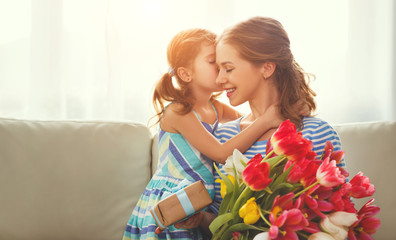 happy mother's day! child daughter   gives mother a bouquet of flowers to tulips and gift