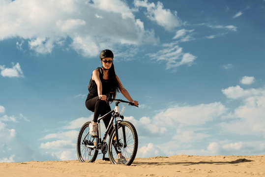 Young lady in sunglasses sitting on top of a mountain with bicycle. Full length image of young female cyclist looking down.