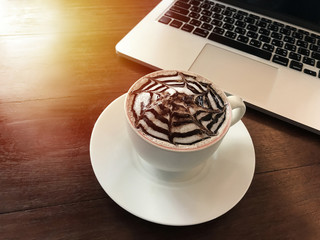 Hot cappuccino white coffee cup with latte art and laptop on wooden table background in cafe. Food and drink concept.	