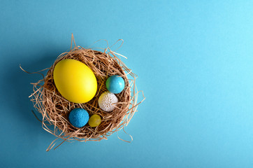 Easter painted eggs with candies in the nest on blue background top view