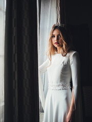 bride near window. white european wedding dress with tiara diadem