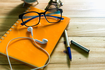 Top view of the desk with notebooks pens glasses headphones and alarm clocks on the table.