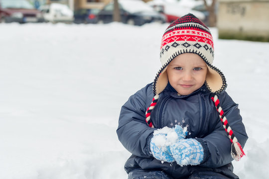 Little boy sitting in snow and playing