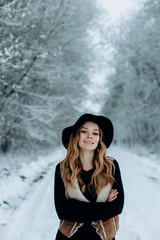 a young stylish woman in a black hat is walking in a winter snowy forest