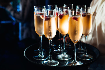 The waiter brings a lot of glasses of champagne and berries