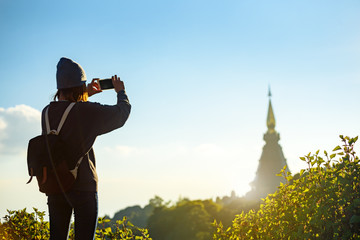 Young female tourist taking picture with smartphone of the ancient temple on mountains , Chiang mai , Thailand