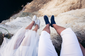 Сouple in love sits on a high cliff near the sea, hanging their legs down. Guy in white breeches and blue sneakers, a girl in net moccasins and an airy white skirt. Look at her feet POV.