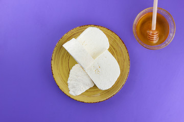 Cheese and honey, Greek cheese on a purple background, feta on a yellow plate, dairy product in a minimalist style, copy space, top view, milk breakfast, wooden cutlery, ultraviolet, honey
