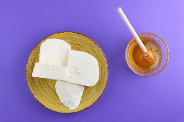 Cheese and honey, Greek cheese on a purple background, feta on a yellow plate, dairy product in a minimalist style, copy space, top view, milk breakfast, wooden cutlery, ultraviolet, honey