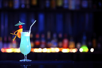 A glass of alcoholic cocktail on a bar counter with colorful bokeh background