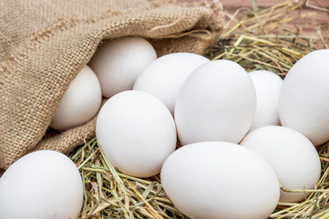 Burlap bag with eggs and hay nest with eggs on wooden background.