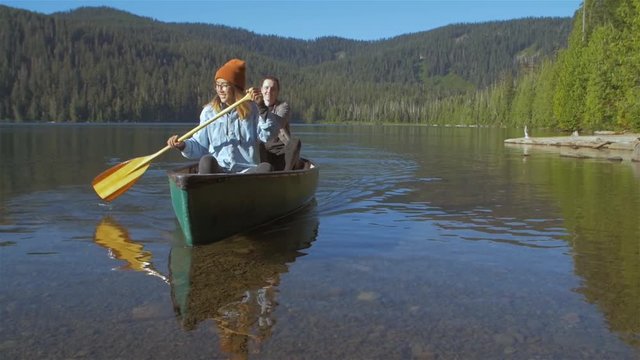 Young loving couple rowing a boat together with some paddles towards the shore on a lake