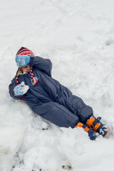 Fototapeta na wymiar Above view of little boy in winter clothes lying on snow