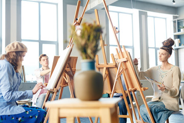 Group of young creative students painting pictures on easels at lesson in school of arts