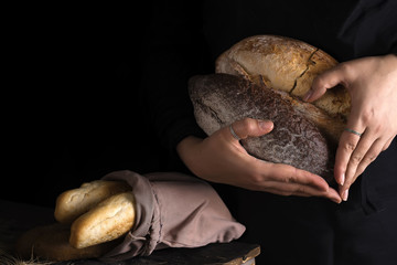 Close-up of woman hands as heart take fresh bread. Dark photo