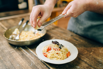 Chef grates cheese in to the plate with fettuccine