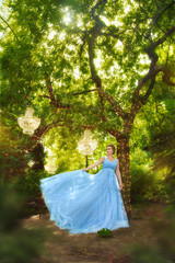 Beautiful woman in blue dress is walking in fairy forest. From above hang crystal chandeliers