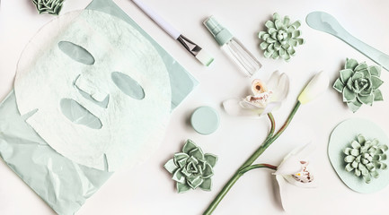 Skin care flat lay with facial sheet mask, mist spray bottle , succulents and orchid flowers on...