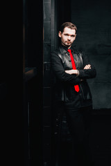 beautiful businessman in a black suit, stands by the window. A young man looks like an executive director or head of a company or enterprise. Room in loft style.