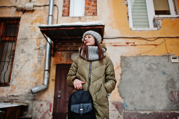Fototapeta na wymiar Portrait of brunette girl in gray scarf and hat, glasses at cold weather against orange wall of old house.