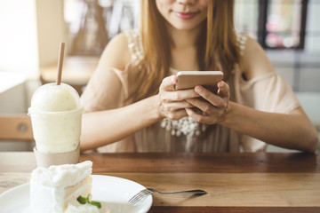 Young woman using smart phone and eating cake in cafe