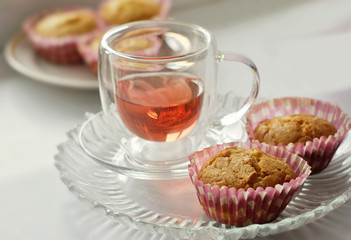 Tea in a glass cup and two homemade cupcakes are on a glass plate. Close-up