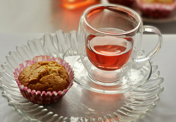 A glass cup of tea and a fresh homemade muffin are on the table