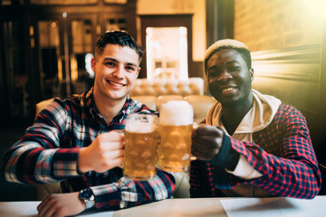 Two best friends or college mates having beer at pub. Afro American man talking to his Caucasian friend in bar