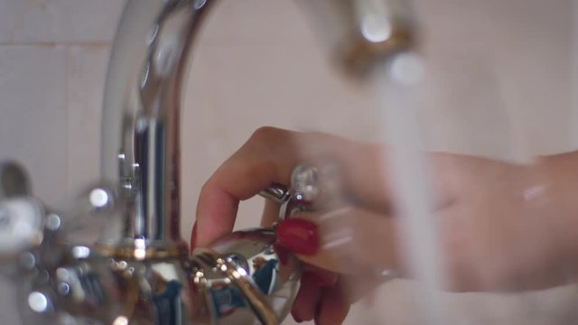 Female Hand Turning Knob On Kitchen Faucet And Pouring Water Into Glass In Bath Room. Close Up Woman Hand Opening Water Faucet And Pouring Water In Glass