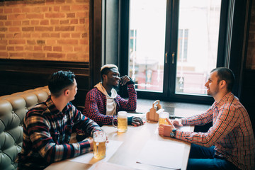 Multiracial friends talking and drinking beer and clinking glasses at pub