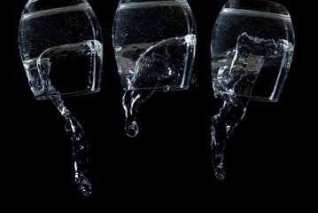 Three inverted transparent glasses with water flowing out of them.