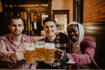 people, men, leisure, friendship and celebration concept - happy male friends drinking beer and clinking glasses at bar or pub