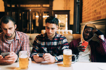 Men's friends with smartphones drinking beer at bar or pub
