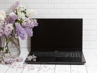 Beautiful white and violet lilac flowers bouquet in glass vase with opened black laptop on the...