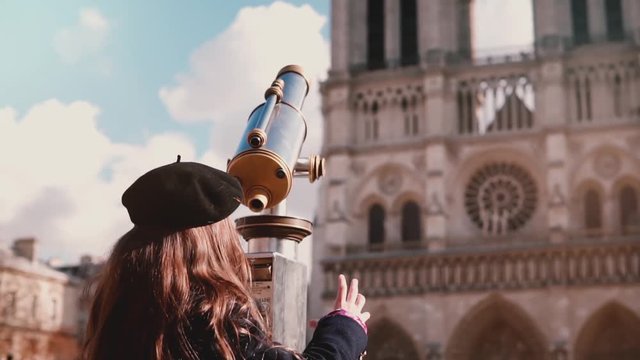 Little girl in beret looks through coin telescope. Slow motion. Notre-Dame de Paris. Child coming up, using tower viewer