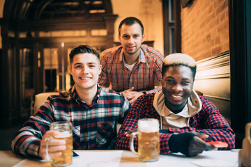 Multiracial friends group drinking and toasting beer at pub. Friendship concept with young people enjoying time together and having fun.