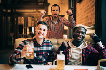 Multiracial men at the pub watcing football game and drinking beer.