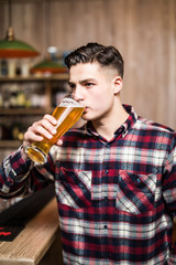 Fototapeta premium Man drinking beer. Handsome young man drinking beer while sitting at the bar counter