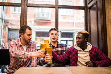 Young happy multiracial men friends drinking beer and talking in pub