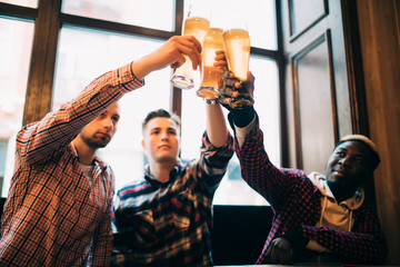 Multiracial friends men cheers with beer in glasses in pub. Toasting beer pub