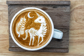 A Cup of coffee with latte art menu which show the unicorn and tree with moon on the wooden table background, drink and art concept