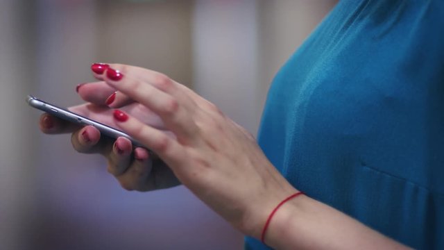 Female hands with red thread touching screen on mobile phone side view. Close up woman hands using mobile app and chatting in social networks