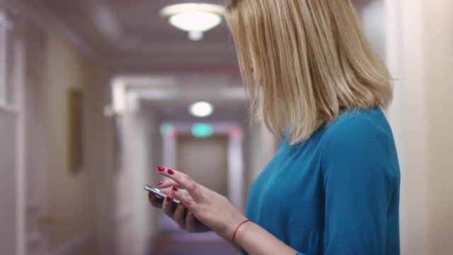 Young woman using smartphone screen for surfing in internet. Blonde woman browsing new mobile app on smartphone in hotel interior. Blonde girl chatting on phone